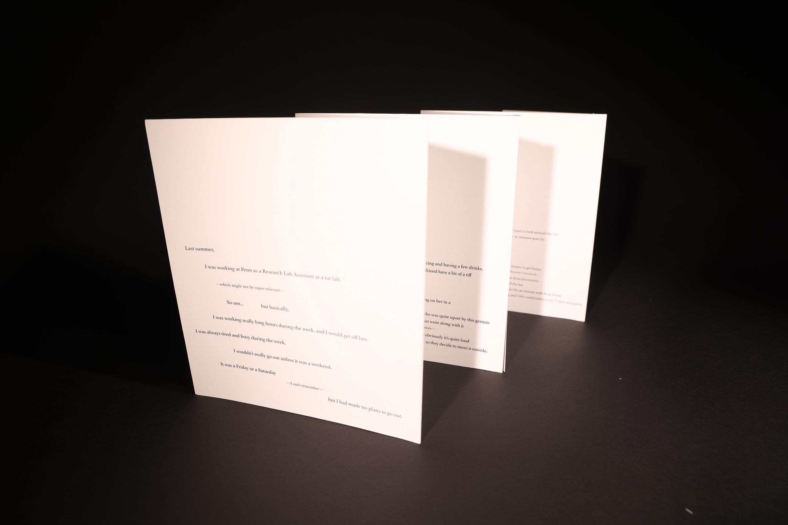 A photograph of the printed piece standing upright on a black surface, its concertina folds opened into a zig-zag so the typographic pages step away from the camera.