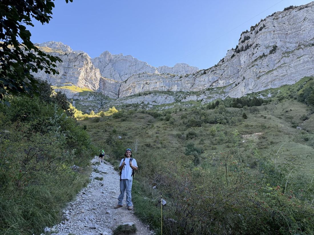 Gabe on a trail through a green valley under tall limestone cliffs.